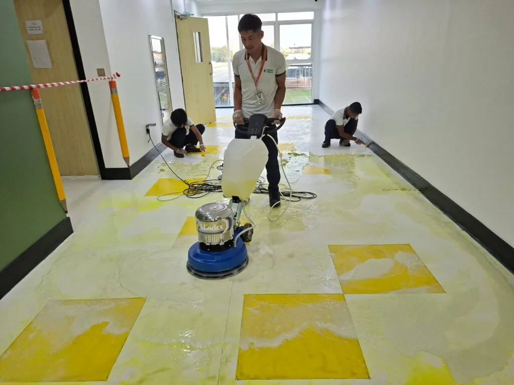 Professional cleaners using a floor scrubbing machine and cleaning tools to perform a deep cleaning service on a yellow and white commercial floor.