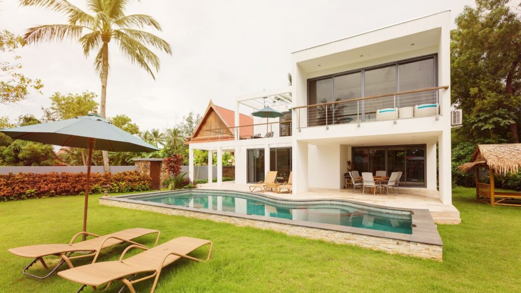 Modern tropical villa with a private pool, sun loungers, and lush green landscaping, ideal for showcasing professional villa cleaning services.
