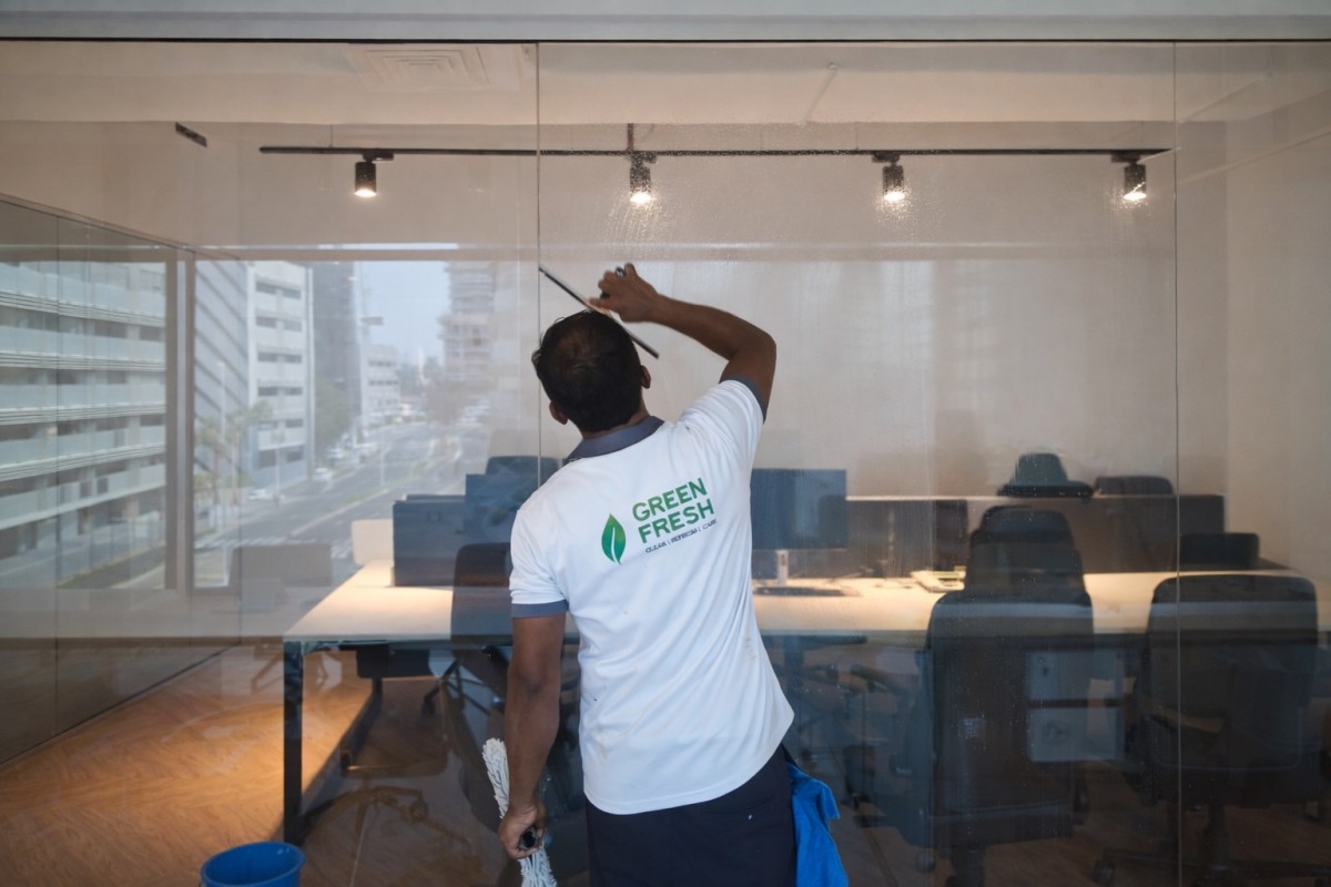 Office Cleaning Service 1 Professional office cleaning services in a Dubai office while cleaning glasses.